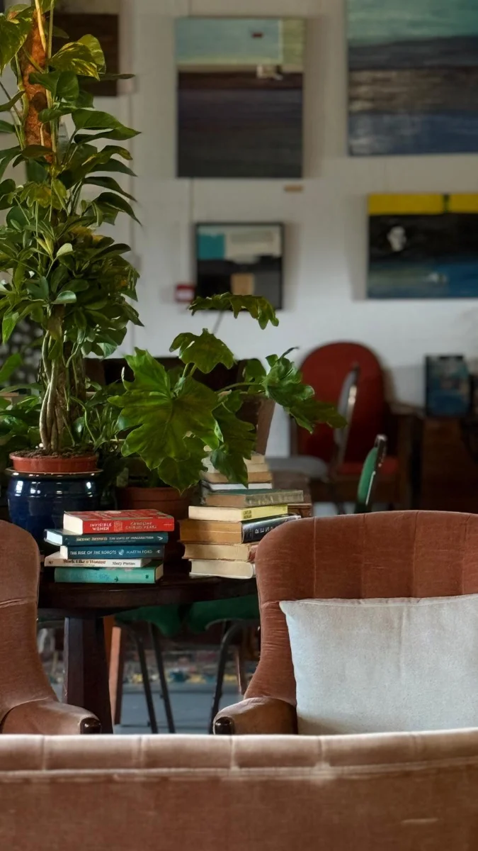 A corner of the cafe with plants, books and armchairs